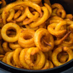 Curly fries in an air fryer basket.