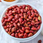 Air Fryer Peanuts in a white bowl with spice mix in a pinch bowl and peanuts scattered around a white cloth.