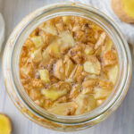 Overhead shot of a ginger bug in a glass jar on a table with chopped fresh ginger.