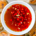 Overhead photo of a bowl of nuoc cham surrounded by summer rolls.