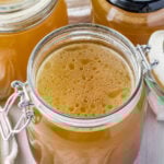 Three jars of ham stock, one with the lid open.