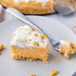 A slice of keto pumpkin cheesecake on a grey plate, with a forkful of cheesecake, next to the whole cheesecake.