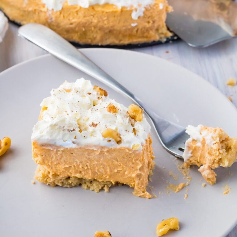 A slice of keto pumpkin cheesecake on a grey plate, with a forkful of cheesecake, next to the whole cheesecake.