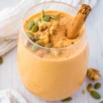 A side shot of a pumpkin smoothie in a small glass with a cinnamon stick.