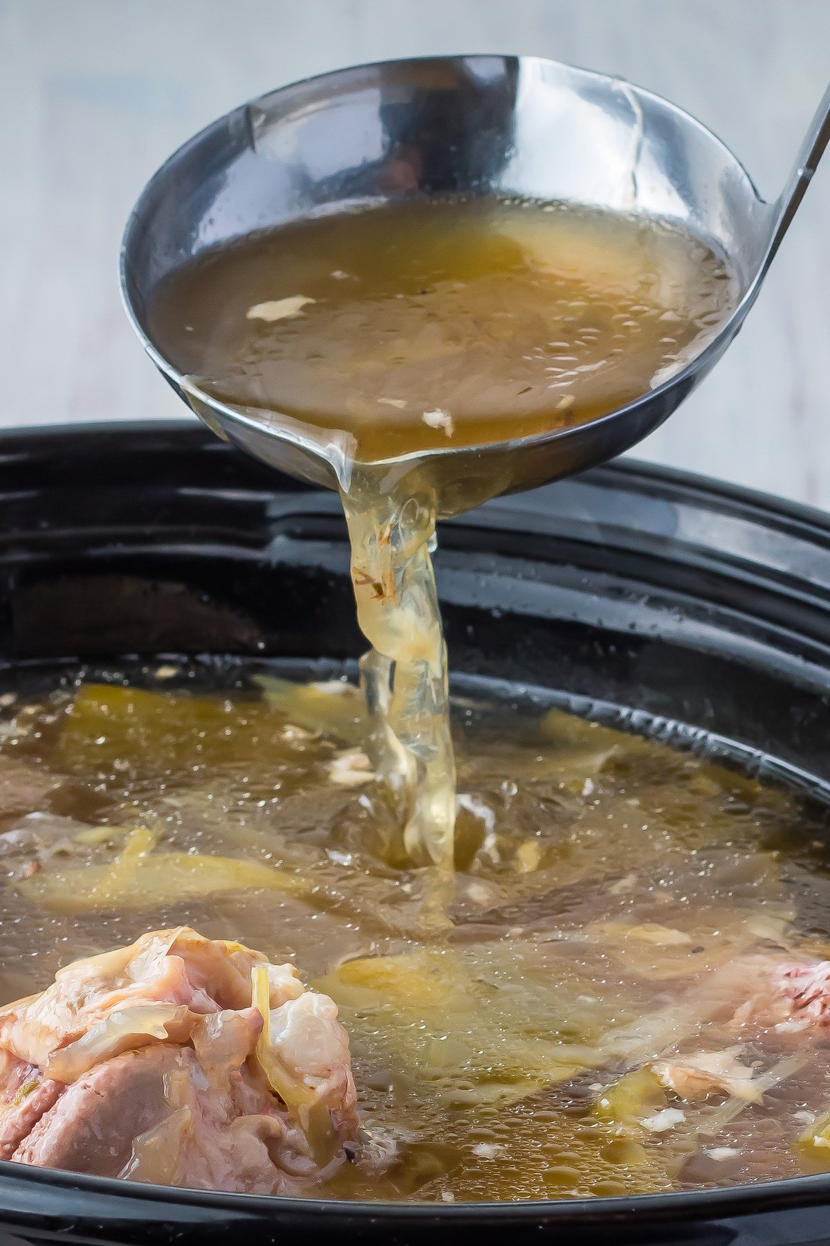 A ladle pouring ham stock into a slow cooker.