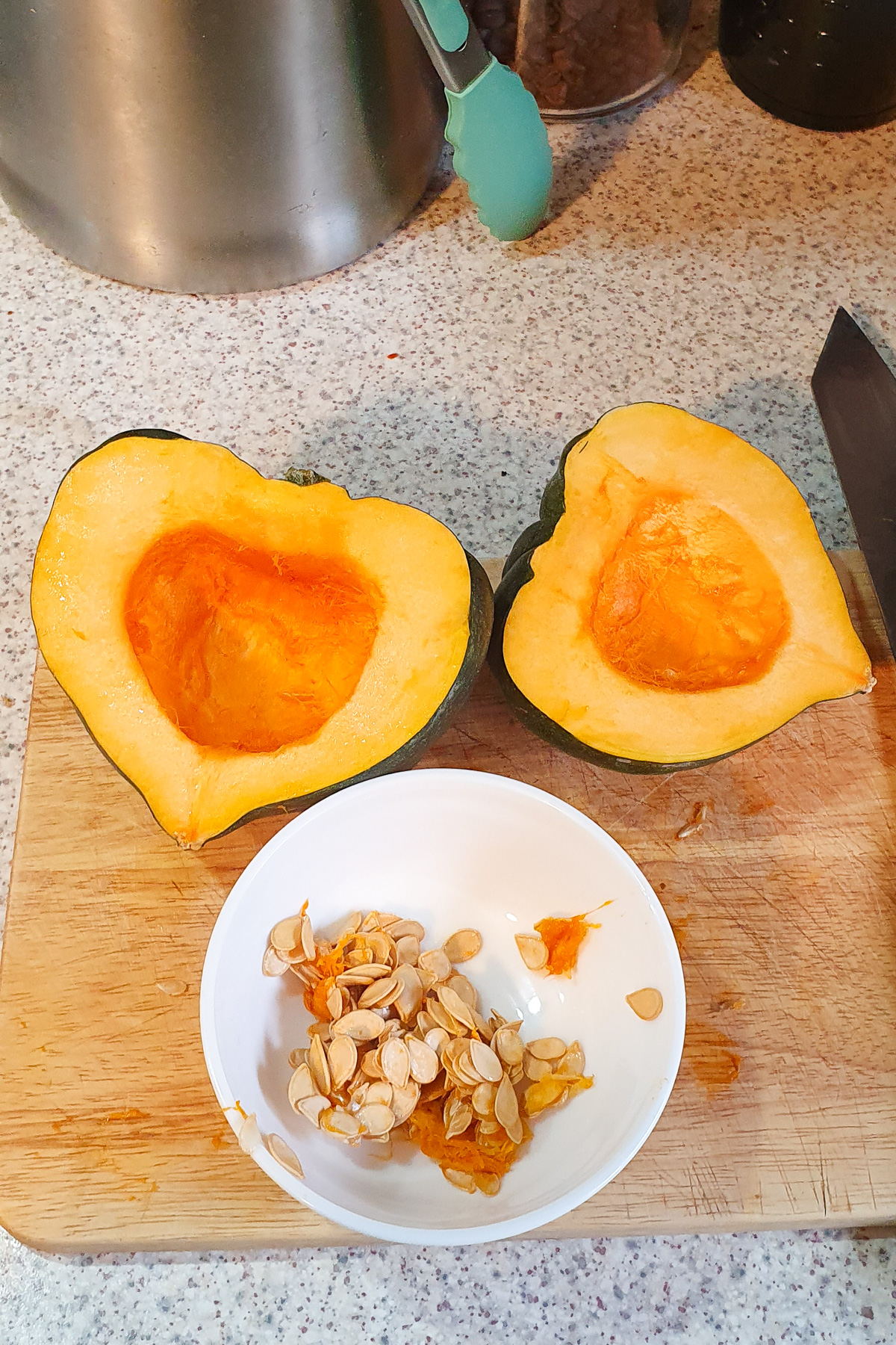 Seeds scooped out of a halved acorn squash and placed in a small white bowl.