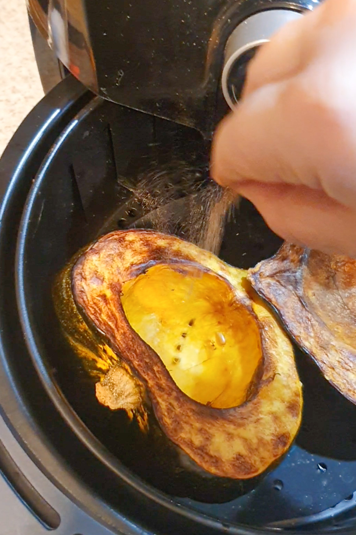 Sprinkling seasoning on an acorn squash in the air fryer.