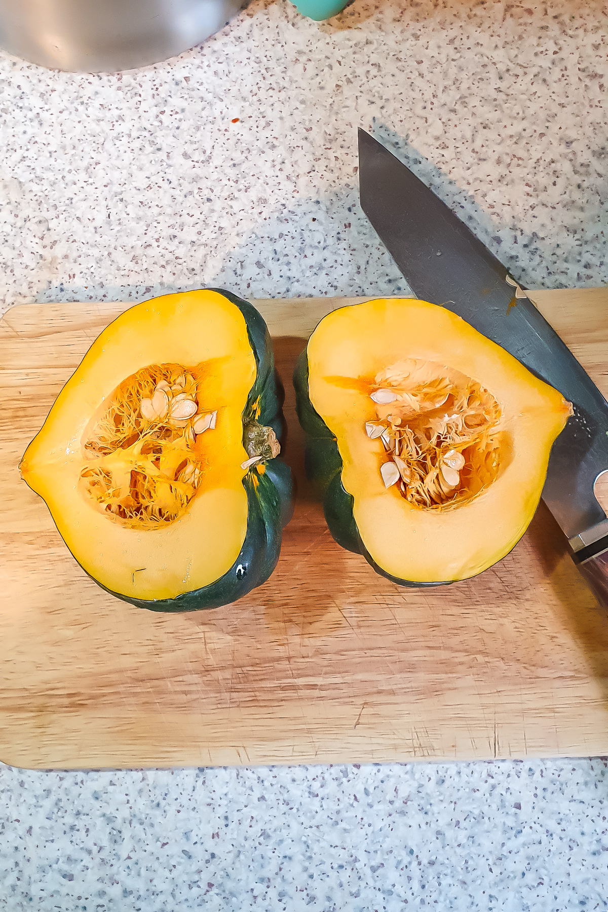 Acorn squash cut in half on a chopping board with a knife.