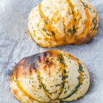 Two roasted carnival squash halves on a baking tray.
