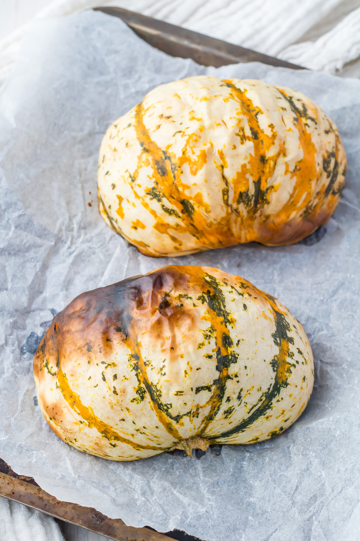 Two roasted carnival squash halves on a baking tray.