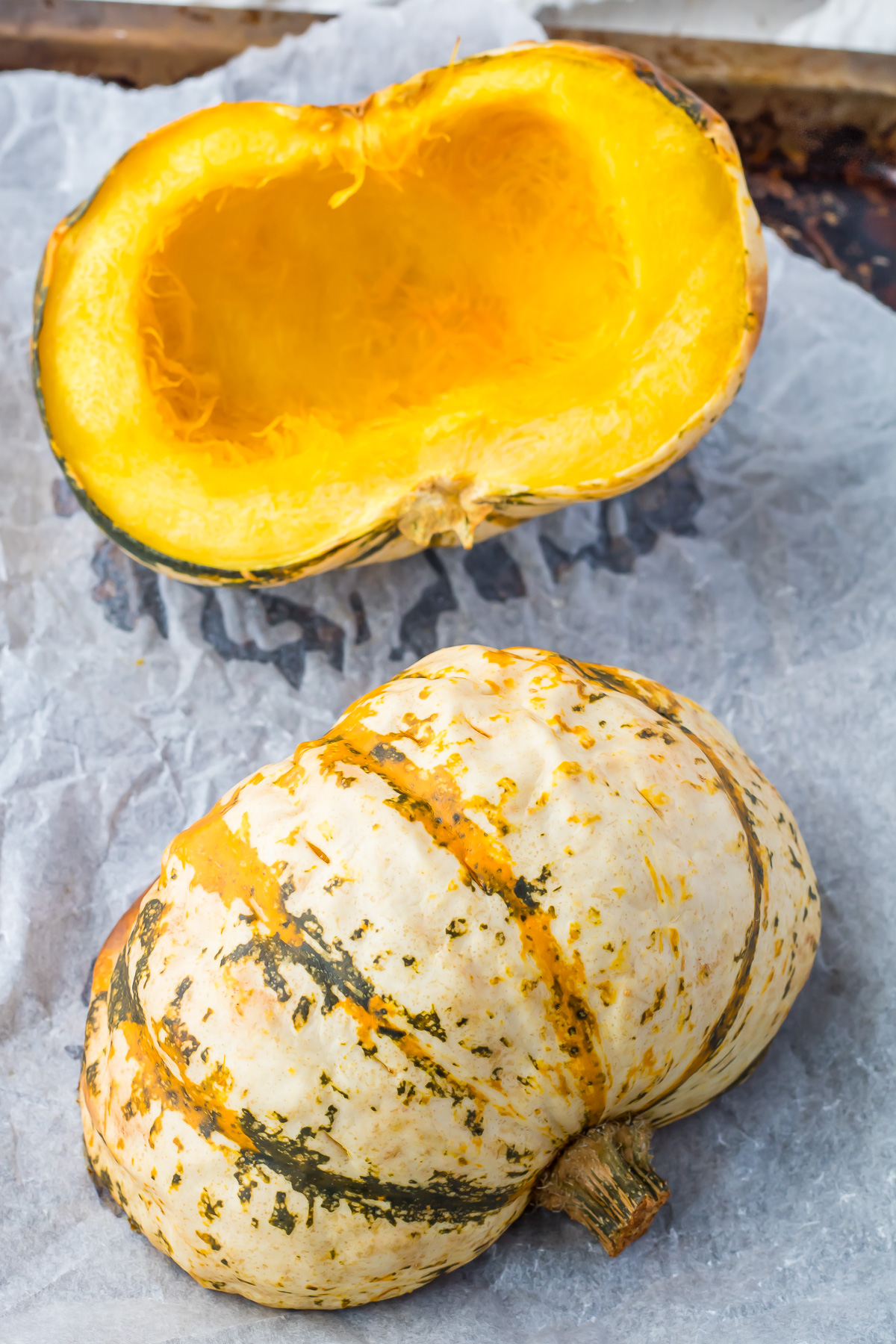 Two roasted carnival squash halves on a baking tray.