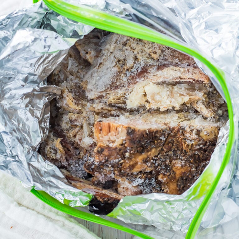 Frozen pulled pork wrapped in foil in a ziplock bag on a table.