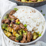 Healthy beef and broccoli in a bowl next to a fork and a frying pan of food.