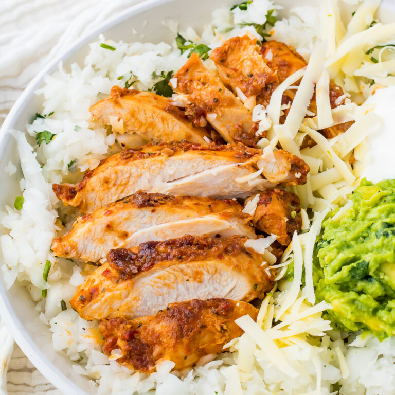 A close-up of a radish rice bowl topped with sliced pollo asado, shredded cheese, and a side of guacamole.