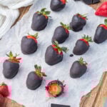 Chocolate-covered strawberries with Nutella arranged on parchment paper, with one berry bitten to show its interior.