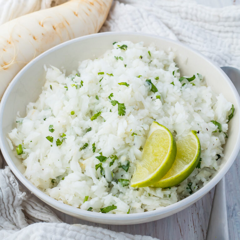 A bowl of cilantro lime radish rice garnished with lime wedges on a wooden table.