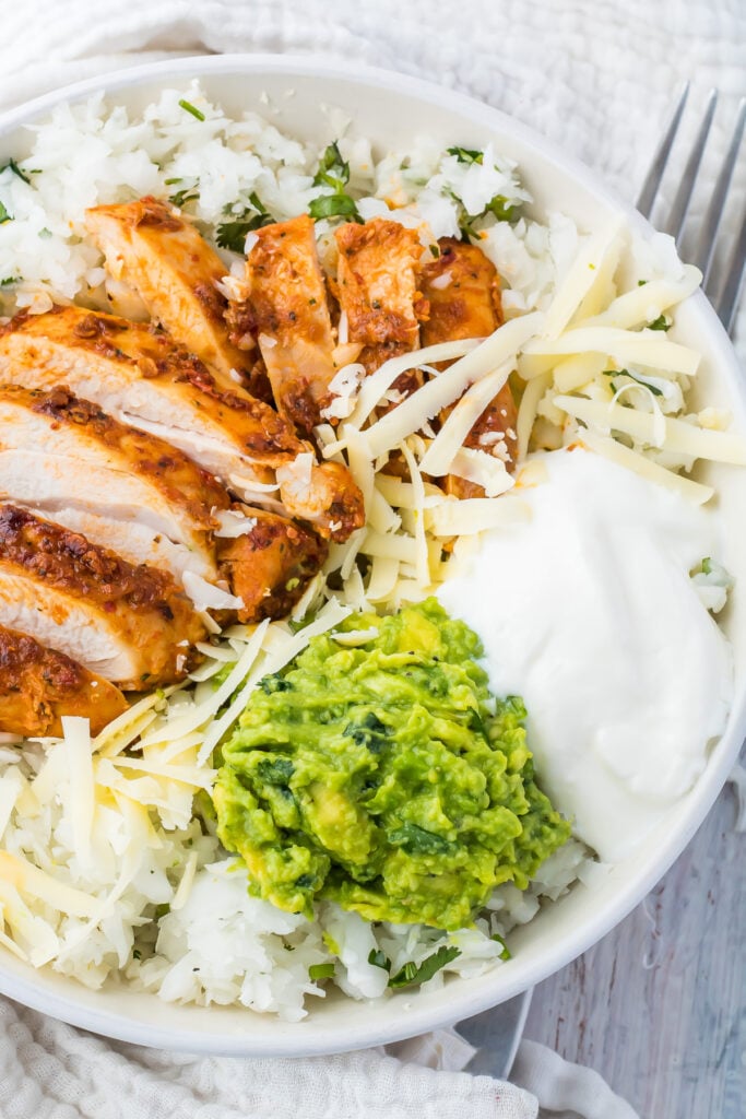 Keto guacamole in a white bowl with radish rice, pollo asado, cheese, and sour cream.