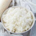 A bowl of freshly cooked radish rice on a wooden table, surrounded by a light gray cloth.