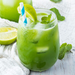 A refreshing cucumber cooler garnished with a lime slice and mint leaves, served with a blue and white striped straw.