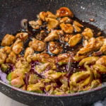 A pan filled with Teriyaki chicken pieces coated in a glossy, rich brown sauce and sprinkled with sesame seeds. The chicken appears tender, with the sauce glistening under the light.