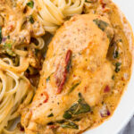 A creamy Tuscan "marry me chicken" dish featuring a tender chicken breast in rich sauce, garnished with sun-dried tomatoes and fresh basil. Served with linguine pasta, all plated neatly on a white dish.