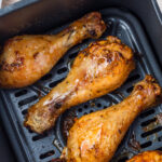 Close-up of three air fryer hot honey chicken drumsticks in an air fryer basket.