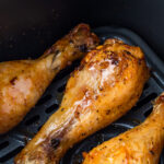Close-up of three seasoned and cooked air fryer hot honey chicken drumsticks in an air fryer basket.