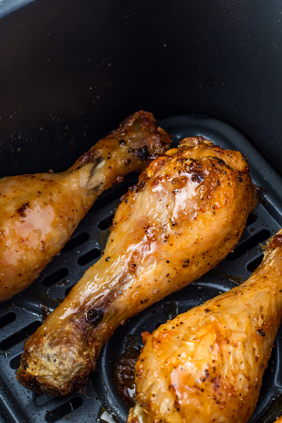 Close-up of three seasoned and cooked air fryer hot honey chicken drumsticks in an air fryer basket.