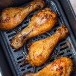 Close-up of three air fryer hot honey chicken drumsticks in an air fryer basket.