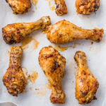 Oven baked drumsticks with a golden, crispy skin are arranged on a sheet of parchment paper. They appear well-seasoned, with visible spices and a slight glaze from their natural juices.