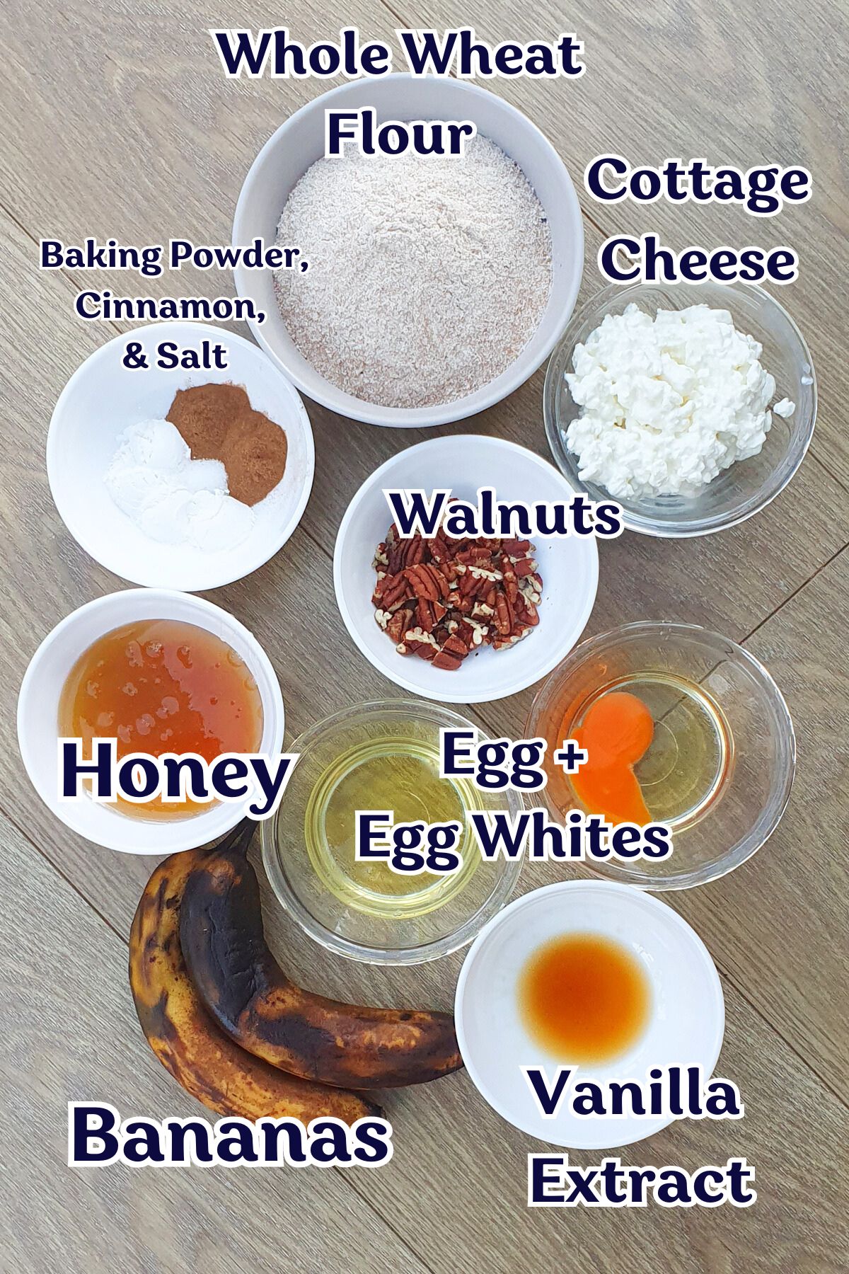 Various baking ingredients in bowls are arranged on a table, including whole wheat flour, cottage cheese, walnuts, honey, eggs, bananas, vanilla extract, and spices.