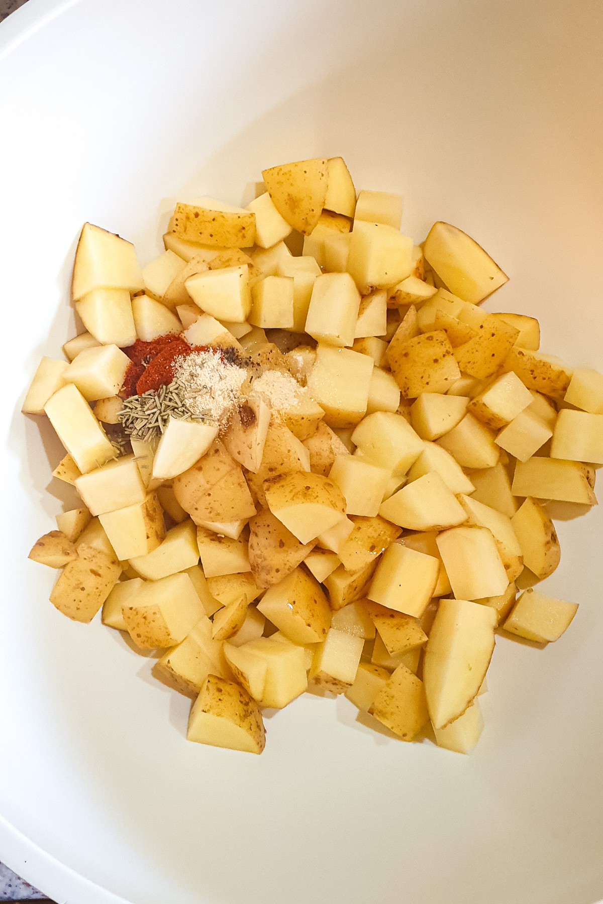 Diced potatoes with various spices and seasonings in a large white mixing bowl.