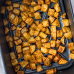 Seasoned diced potatoes are evenly spread inside an air fryer basket, appearing golden brown and roasted.