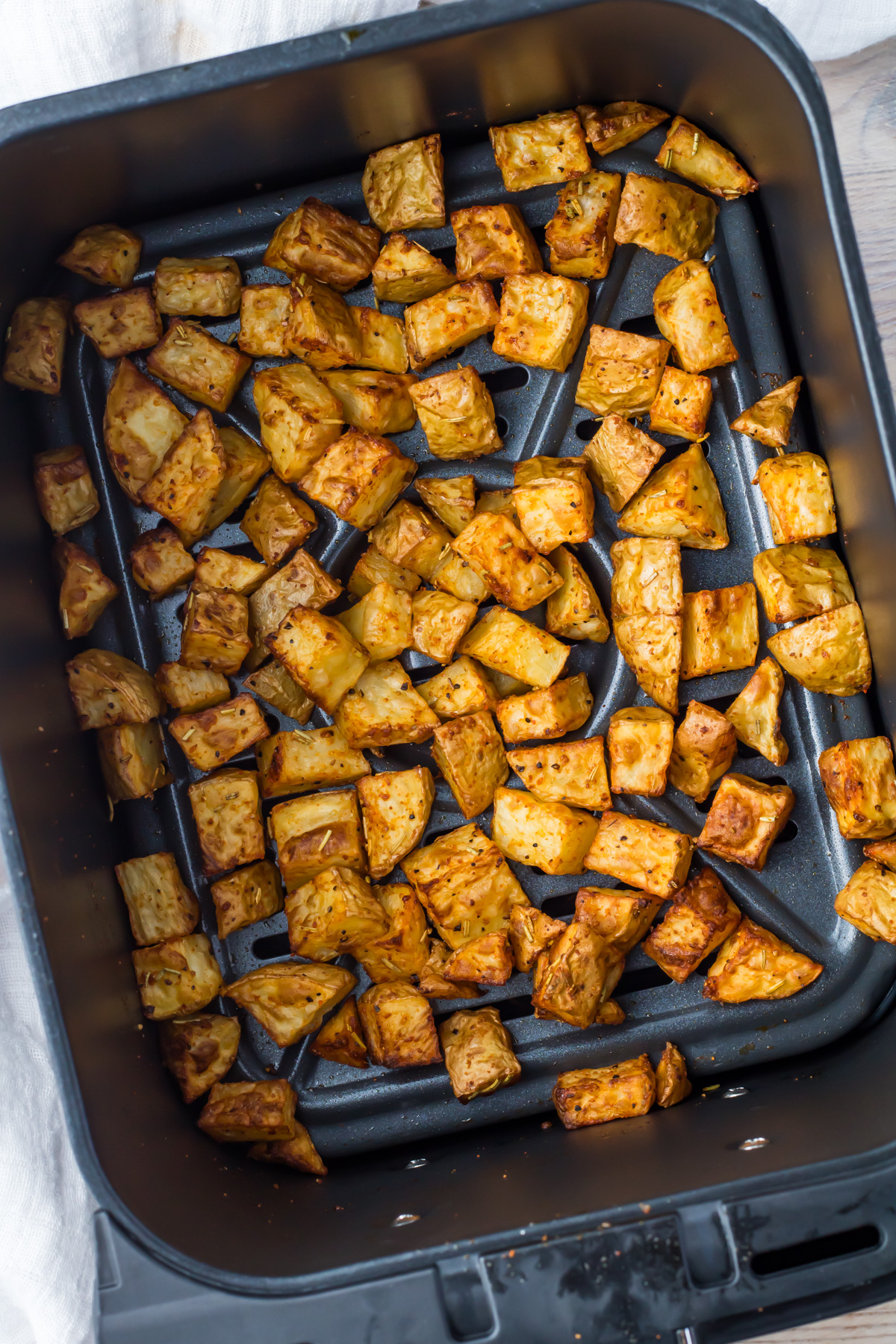 Seasoned diced potatoes are evenly spread inside an air fryer basket, appearing golden brown and roasted.
