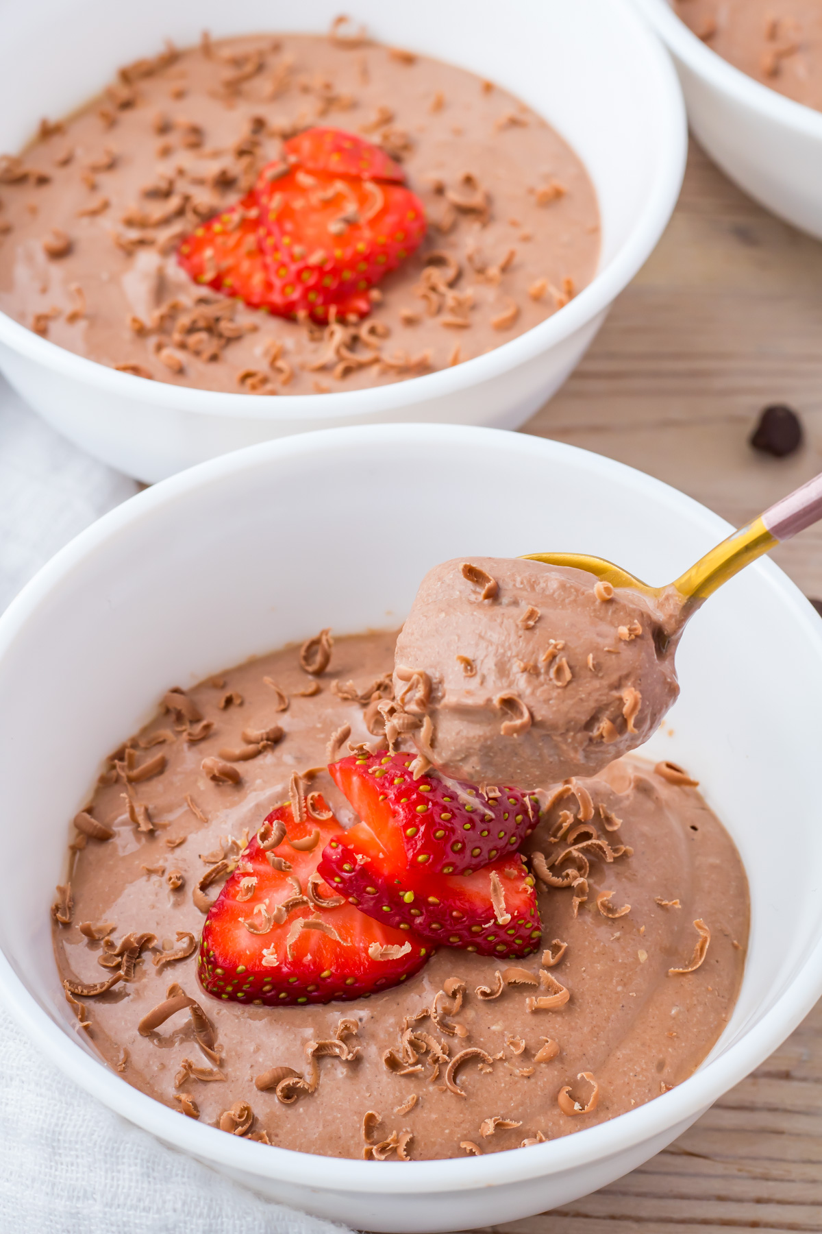 Bowl of chocolate cottage cheese mousse topped with sliced strawberries and chocolate shavings, with a spoonful being lifted from the bowl.