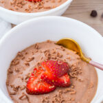 A white bowl filled with chocolate cottage cheese mousse, topped with sliced strawberries and chocolate shavings, with a gold spoon on the side.