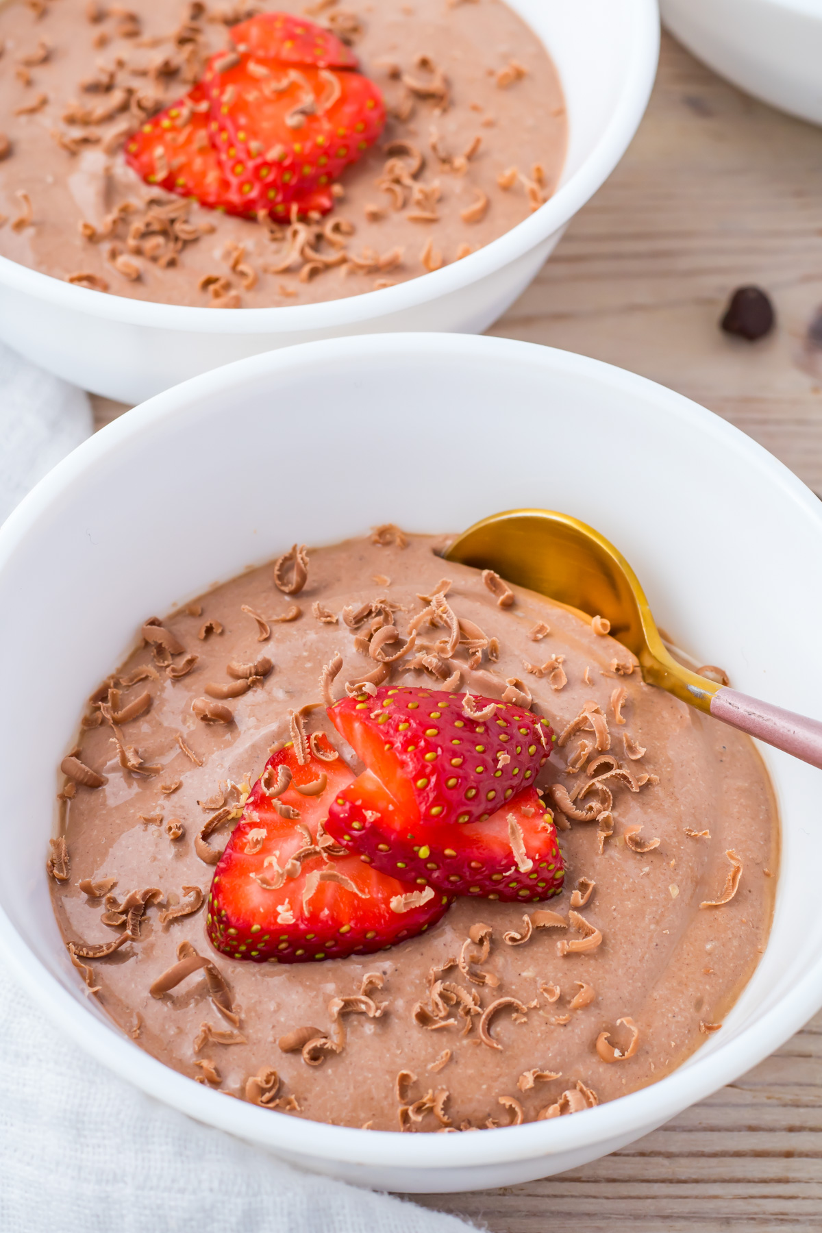 A white bowl filled with chocolate cottage cheese mousse, topped with sliced strawberries and chocolate shavings, with a gold spoon on the side.