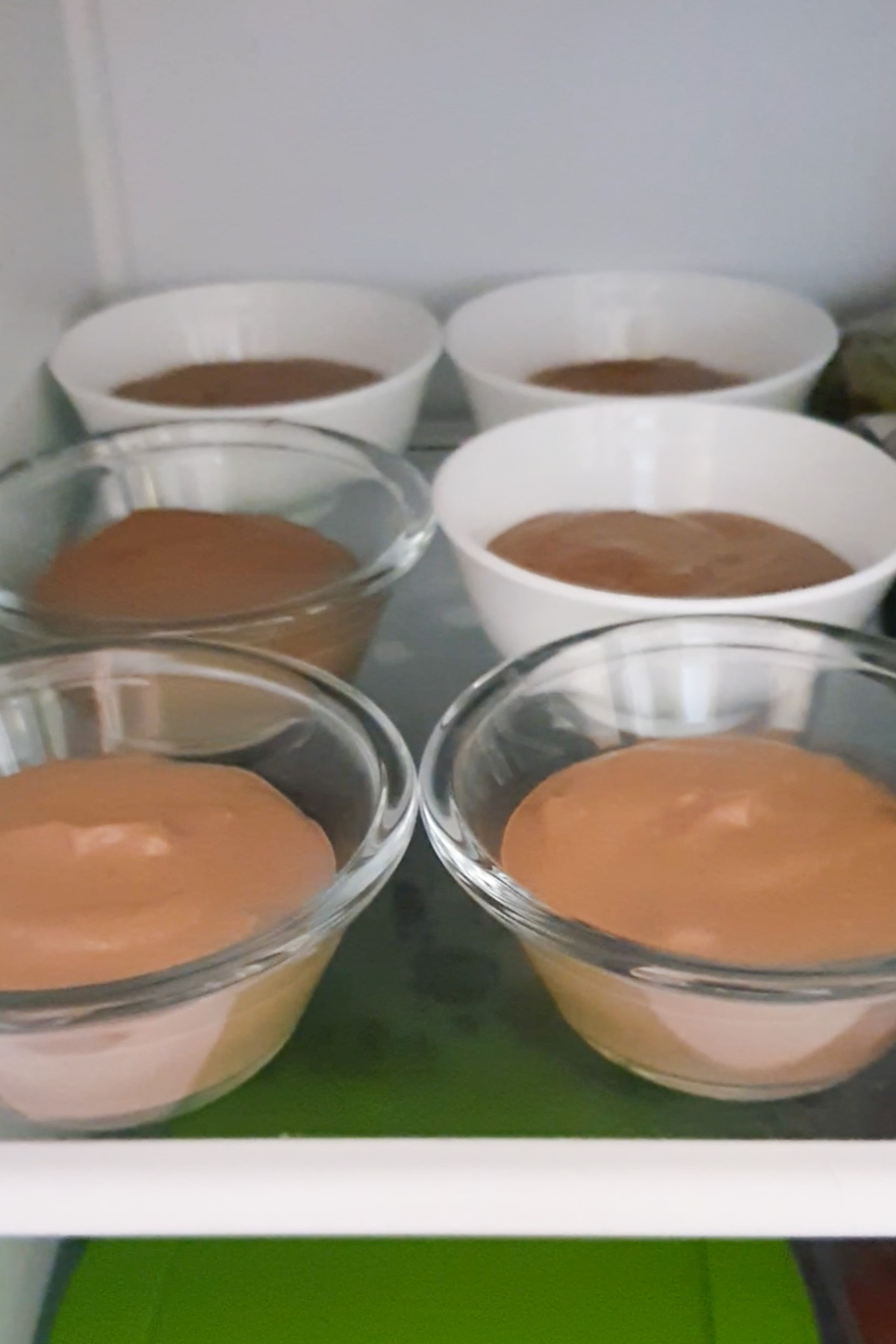 Six bowls of cottage cheese mousse, three in clear glass bowls and three in white ceramic bowls, arranged in a refrigerator.