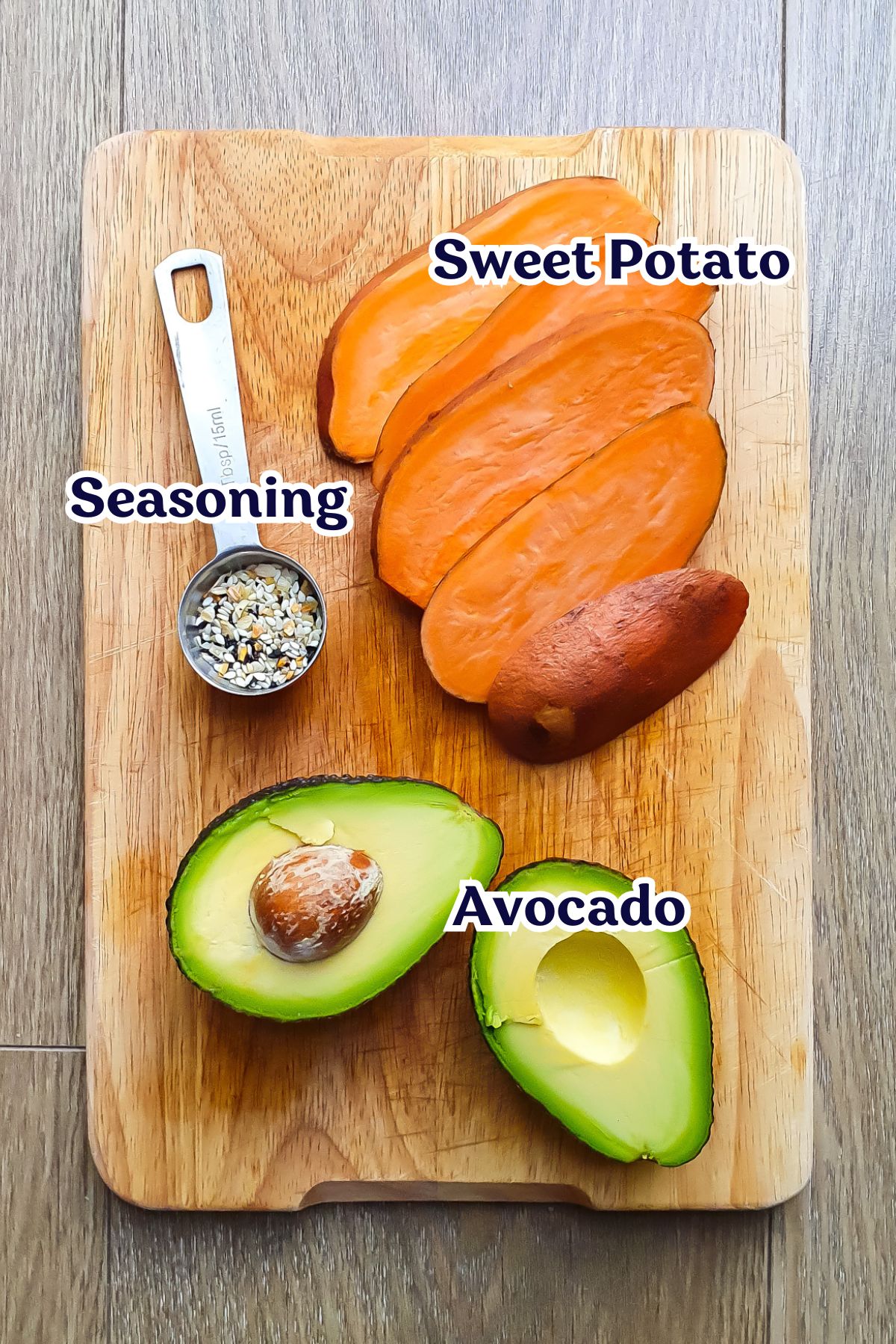 A wooden cutting board with sliced sweet potato, a halved avocado with pit, and a metal spoon of mixed seasoning, each labeled accordingly.