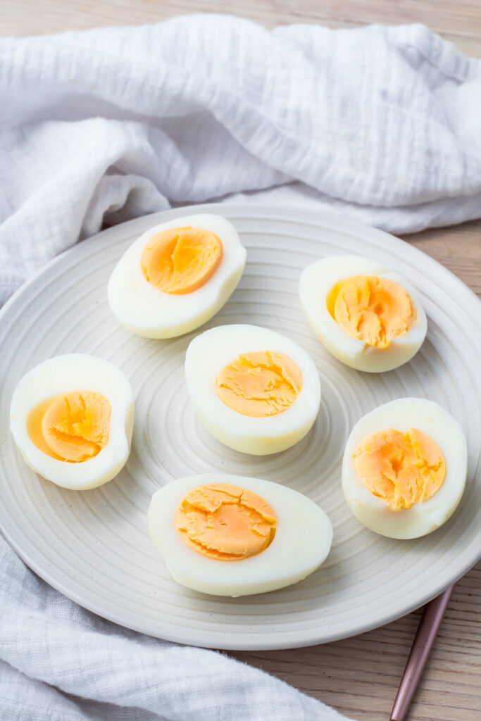 A plate with seven halved air fryer hard boiled eggs sits on a light surface, with a white cloth in the background.