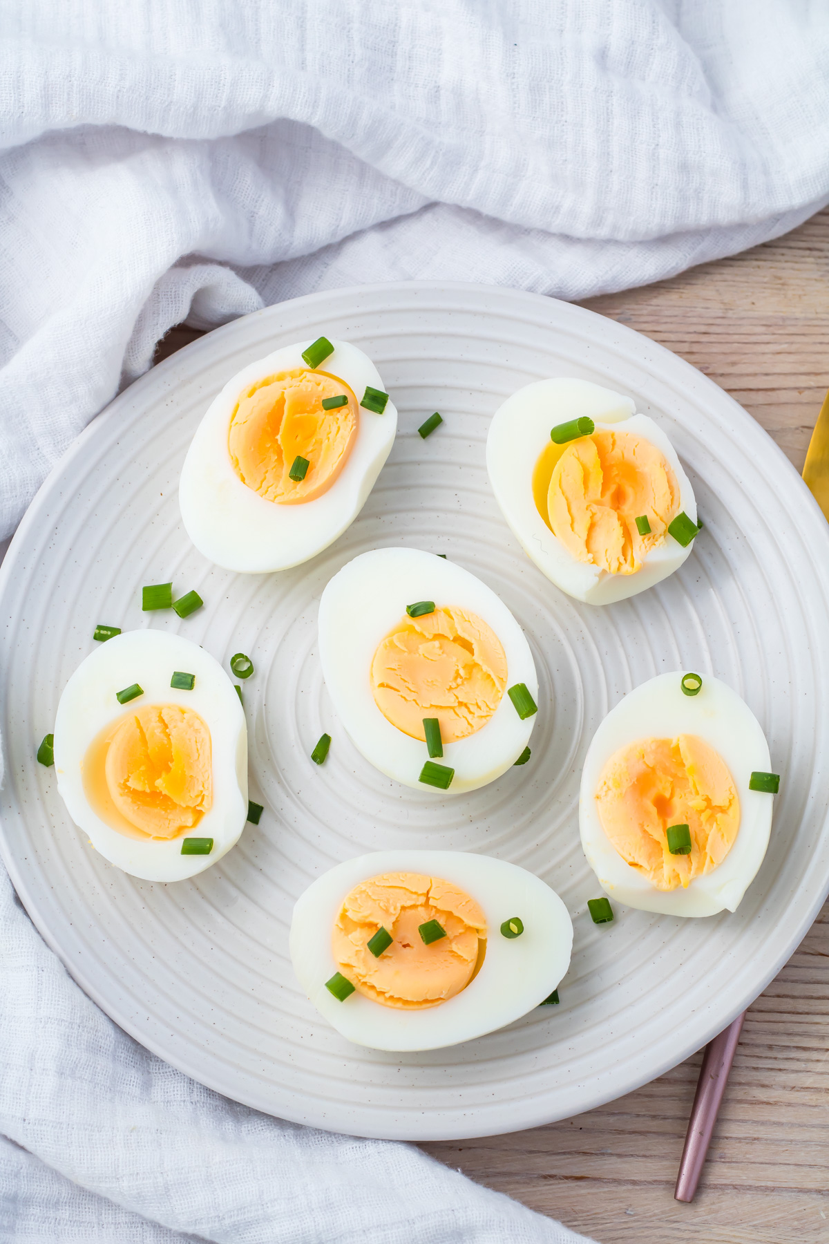 A plate with six halved air fryer hard-boiled eggs, garnished with chopped green onions, on a light-colored cloth and wooden surface.