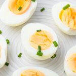 Halved air fryer hard boiled eggs arranged on a white plate, garnished with chopped green onions.