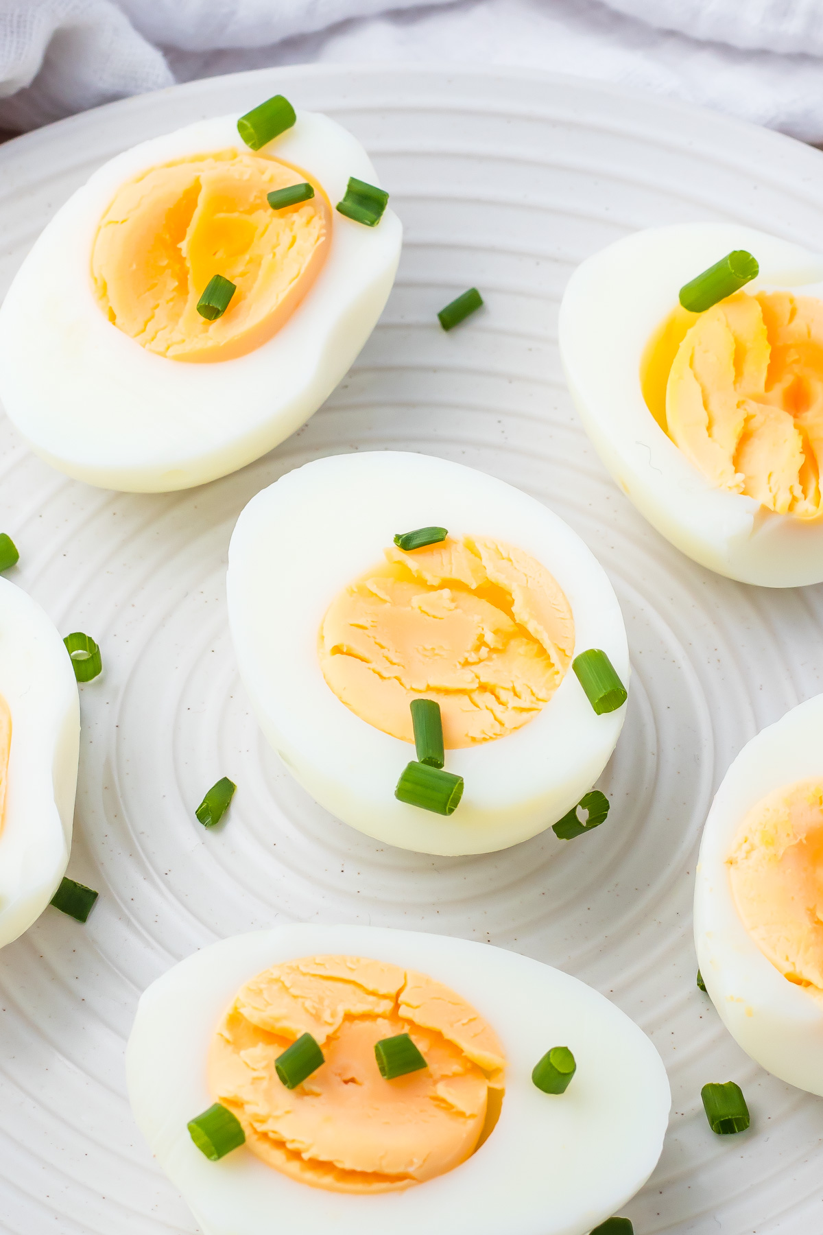 Halved air fryer hard boiled eggs arranged on a white plate, garnished with chopped green onions.