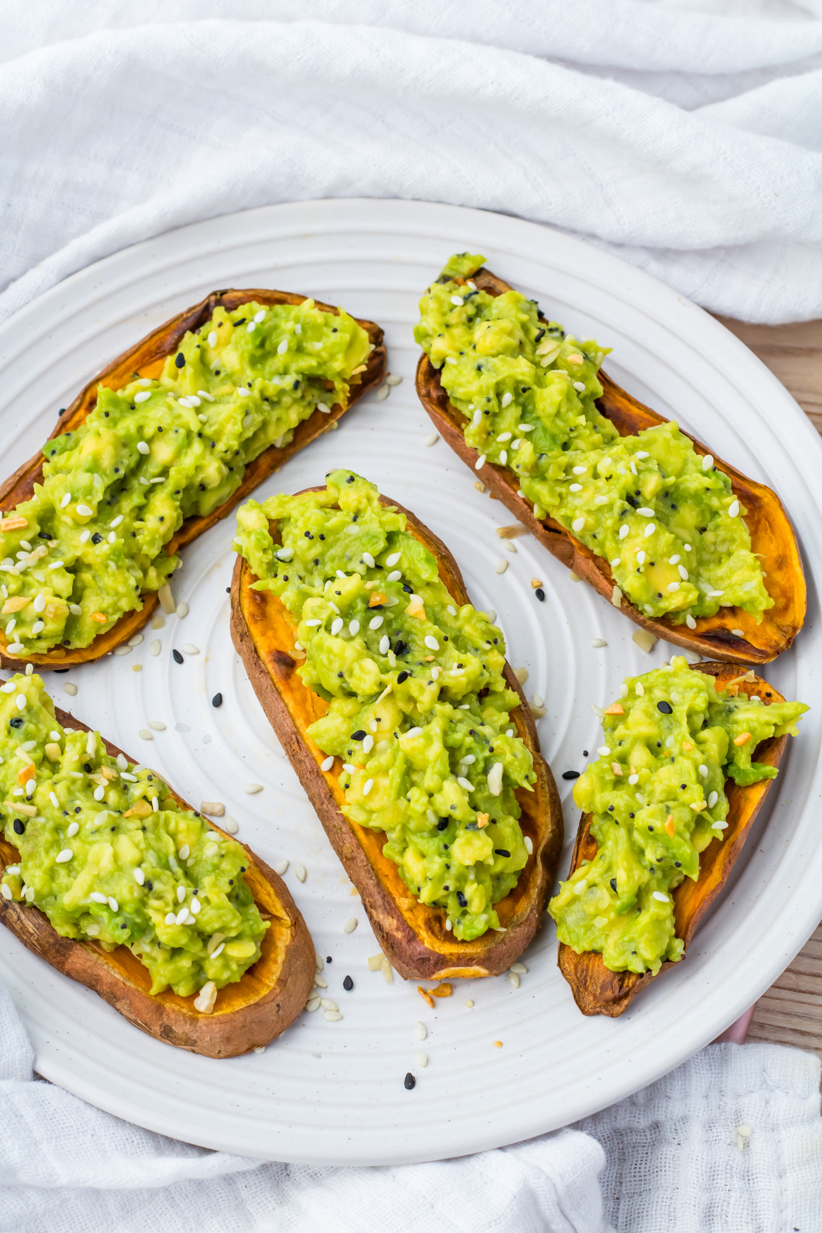 Five sweet potato avocado toast slices sprinkled with sesame seeds on a white plate.