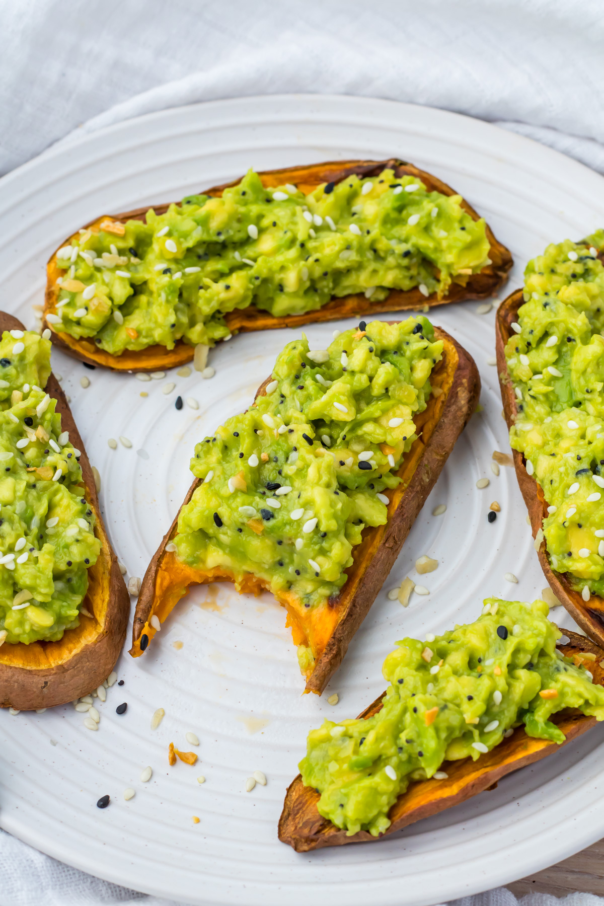 Slices of sweet potato avocado toast sprinkled with sesame seeds on a white plate.