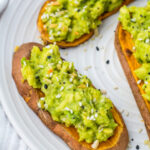 Slices of sweet potato avocado toast sprinkled with sesame seeds on a white plate.