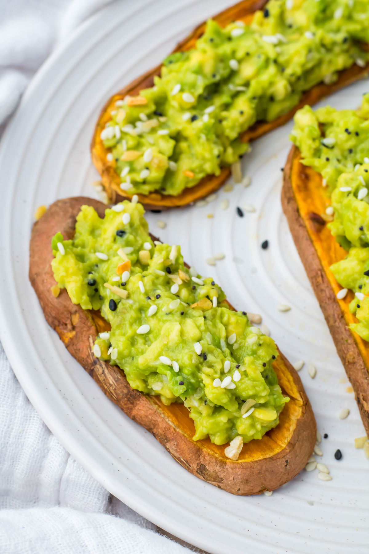 Slices of sweet potato avocado toast sprinkled with sesame seeds on a white plate.