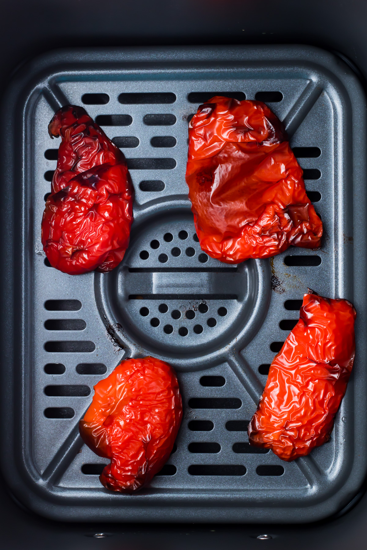 Four air fryer roasted red bell pepper halves on the tray of an air fryer.