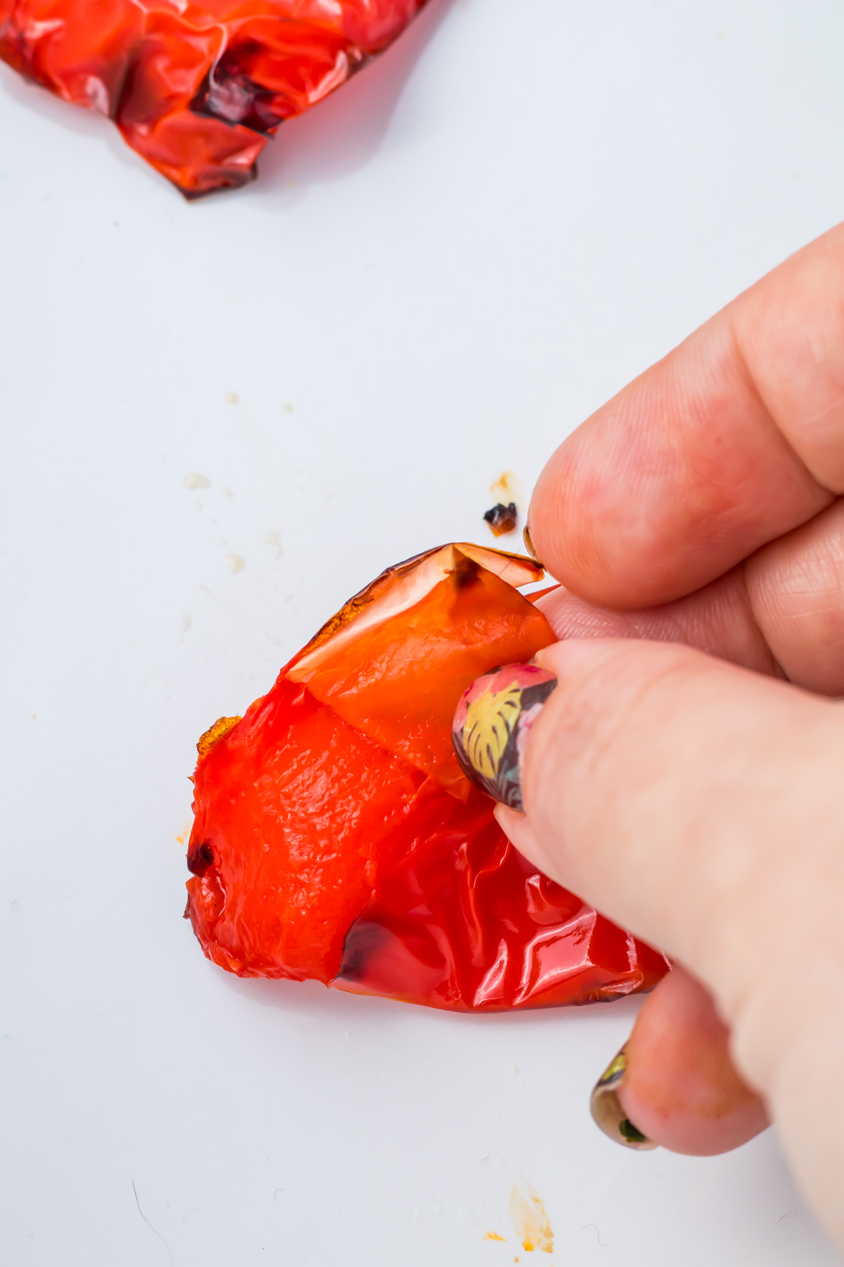 A hand peels the charred skin off a roasted red bell pepper on a white surface.