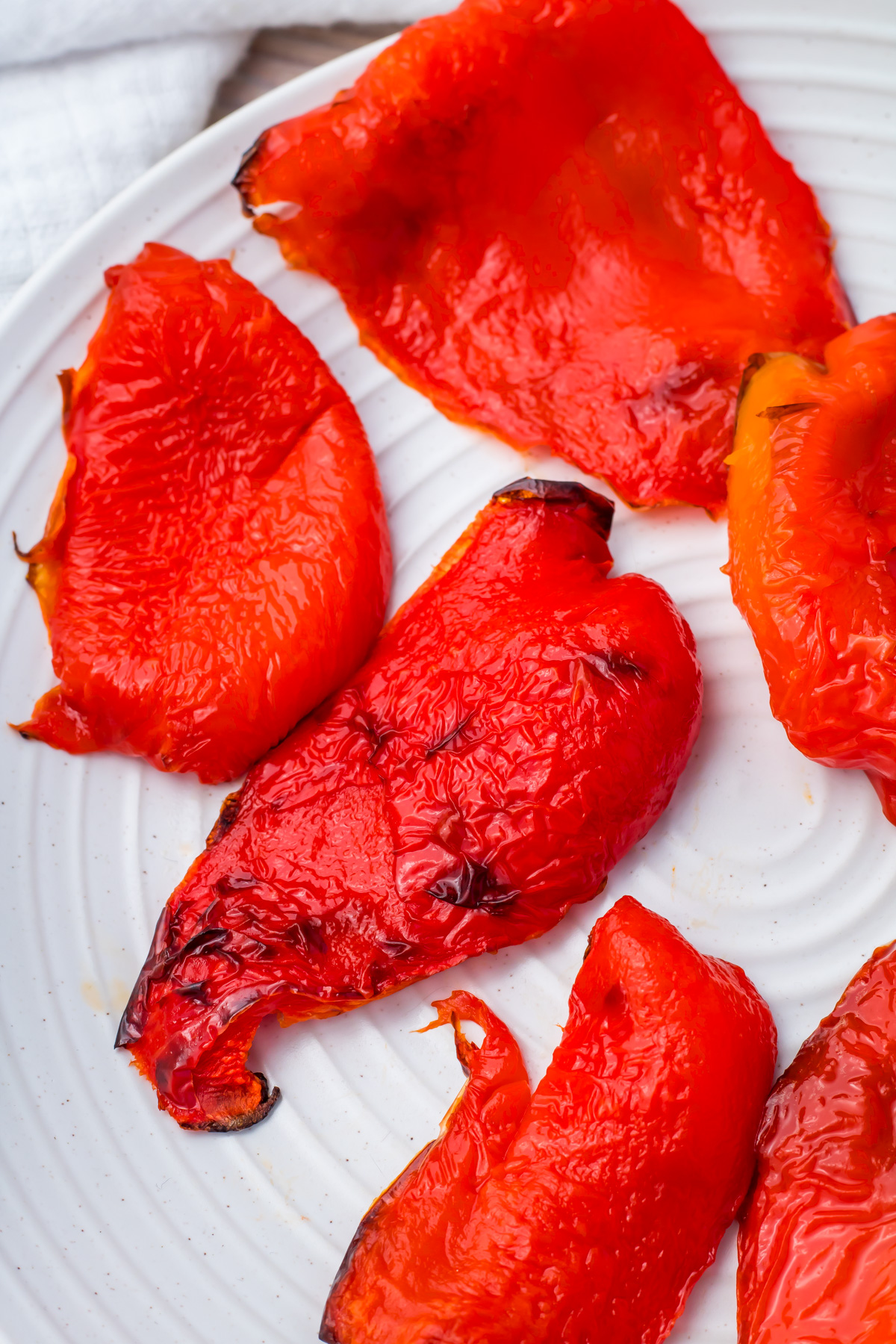 Several pieces of roasted red bell pepper with slightly charred skins are arranged on a white plate.